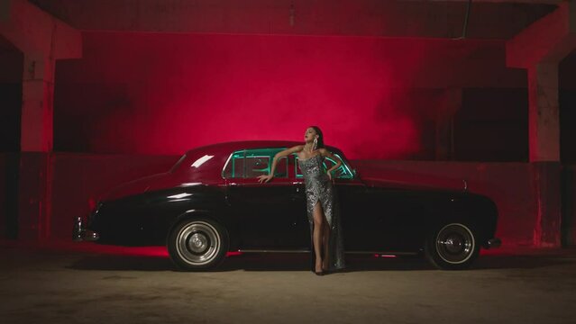 Beautiful Elegant Young Woman Standing , Dancing and Flirting near old retro classic car. Old fashioned luxury style concept . Rich fashion lifestyle . Luxury dress with fabric glitter, spangles .