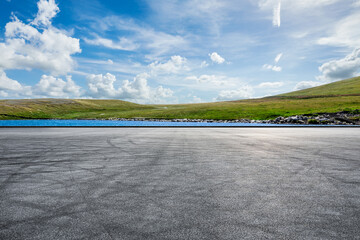 Empty asphalt road and lake with green grass under blue sky - Powered by Adobe
