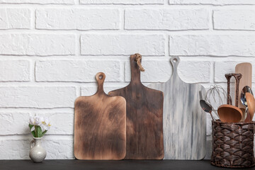 Kitchen utensils, cutlery, crockery, wooden cutting boards on a white brick wall background front view