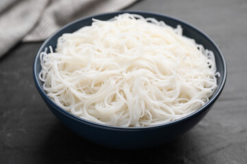 Bowl with cooked rice noodles on black table, closeup