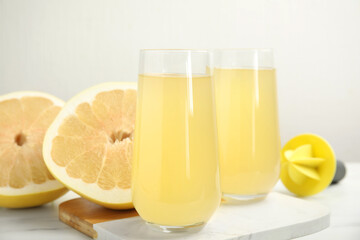 Glasses of fresh pomelo juice and fruit on white table