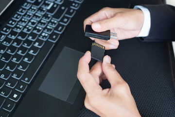 Hand with black suit holding memory sd card and card reader for copy data from camery to laptop...