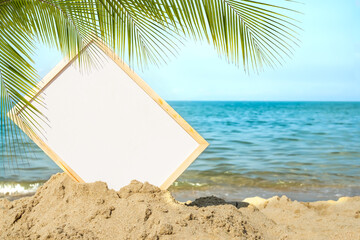Mockup white board on sand beach with leaves palm or coconut palm at coast on blur blue sea and blue sky. card or poster for tourism vacation travel tropical summer in holidays.nature landscape ocean.