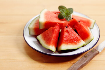 Fresh red watermelon slices in white plate on wooden background.