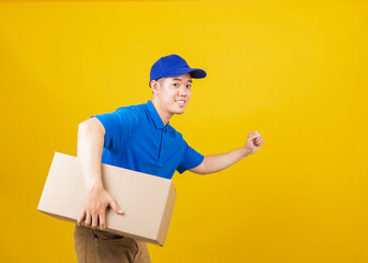 Portrait excited delivery happy man logistic standing smile wearing blue t-shirt and cap uniform holding parcel box and running looking to camera, studio shot isolated on yellow background, side view