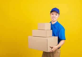 Portrait excited attractive delivery happy man logistic standing he smile wearing blue t-shirt and cap uniform holding parcel box looking to camera, studio shot isolated on yellow background
