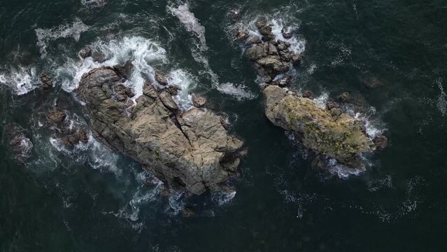 Waves crashing onto a small, rocky island in the vast and deep blue ocean off Manuel Antonio Beach on the Central Pacific Coast of Costa Rica. Aerial top down view