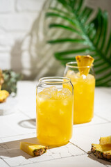 Pineapple cocktail or juice in two glasses with ice on white background with palm leaves