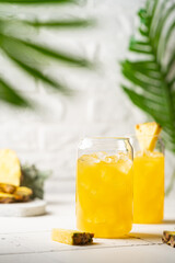 Pineapple cocktail or juice in two glasses with ice on white background with palm leaves