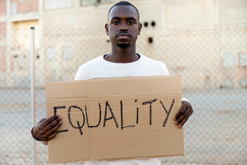 Young African American man looking at camera holding cardboard sign: Equality. Human rights...