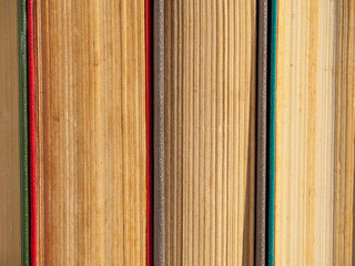 Abstract textured background of pages of closed hardcover books. Old battered books with yellowed pages from time close-up. Close-up of old books standing side by side on a bookshelf