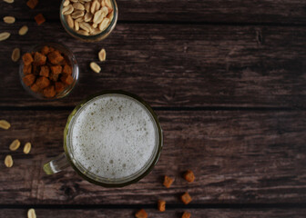 light beer in a glass mug with crackers and peanuts on a dark background