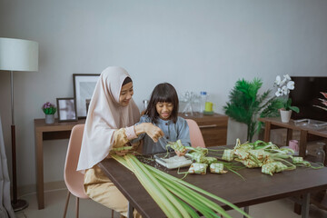 muslim mother and daughter make ketupat for eid mubarak