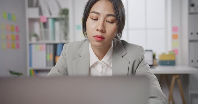 Young Asian businesswoman sit on desk with laptop overworked tired burnout syndrome at office. Exhausted lady with sleeply eye at workplace, Girl not enjoy unhappy with work, Work mental health.