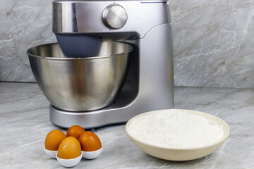 Modern kitchen machine and ingredients for preparing dough (eggs and flour) on a kitchen table