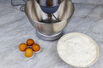 Modern kitchen machine and ingredients for preparing dough (eggs and flour) on a kitchen table