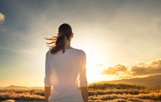 Life is beautiful. Woman standing facing a beautiful golden sunrise enjoying a peaceful moment in nature 	
