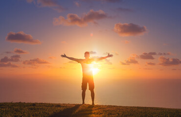 Man relaxing in a field enjoying nature with arms outstretch up to the sunrise. Feelings of hope, worship  and happiness 