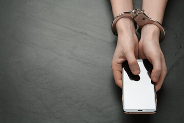 Man in handcuffs holding smartphone at black table, top view. Internet addiction