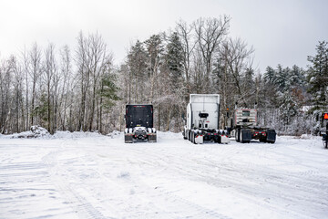 Different big rigs semi truck tractors without semi trailers standing in row on winter snow and ice...