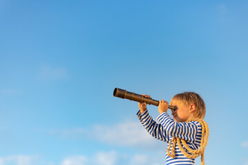 Happy child looking through vintage spyglass against blue sky.