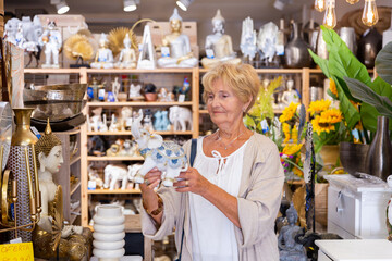 Focused mature woman looking for decorative statue at household store