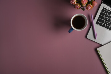 Cup of coffee, laptop computer, notebook and flower pot on purple background.