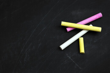 Colorful chalks on black board, flat lay. Space for text