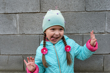 A girl grimaces against a gray wall. A five-year-old child with long hair braided into pigtails. A...