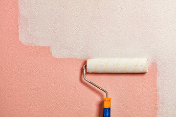 A paint roller paints a coral colored wall with white paint. Close-up.