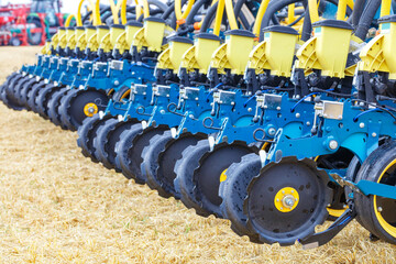 A row of wheels with a pneumatic distribution mechanism and pipes on a multi-row planter against the backdrop of an agricultural field. - obrazy, fototapety, plakaty