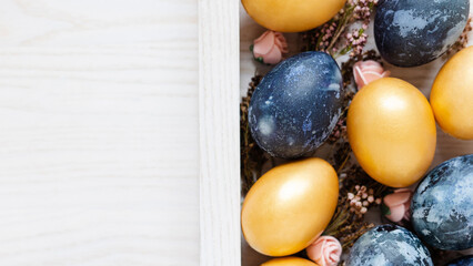 easter wooden background with golden and dark blue eggs and dried flowers with empty space for text top view