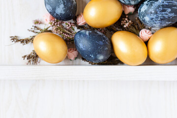 easter wooden background with golden and dark blue eggs and dried flowers with empty space for text top view
