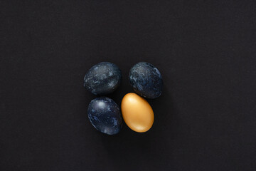 Fototapeta na wymiar four easter eggs in blue and gold on a black paper background, conceptual easter minimalism
