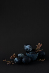 still life of six Easter eggs and dried flowers on black paper background, Easter composition with black copyspace