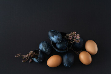 composition of nine Easter eggs and dried flowers on black dark background, Easter still life in...
