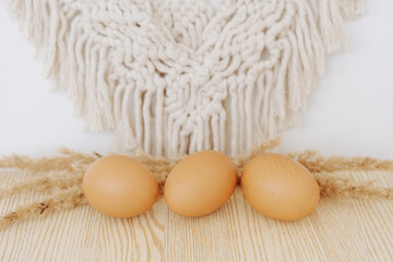 Fototapeta na wymiar three yellow chicken eggs with ears on wooden box and macrame, natural farm eco eggs