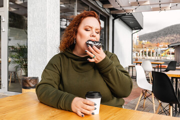 Portrait of overweight enjoing woman eating a chocolate donut at cafe. The concept of diet and body...
