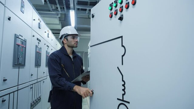 Electrical engineer using digital tablet inspect and program for electric power system in electrical control room. Engineer male working at factory. Concept of industry, factory, renewable energy.