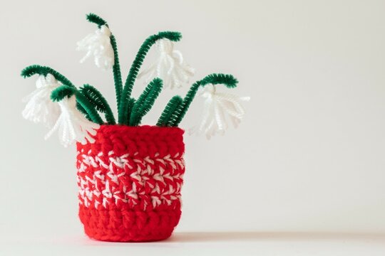Close up red and white yarn strains of crochet vase and tassel snowdrops flowers as martenitsa, Bulgarian folklore tradition in march, Baba Marta day. Shallow depth, copy space on light background.