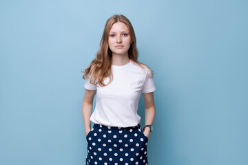 Headshot portrait happy young woman in white t-shirt and polka dot skirt smiling posing while looking at camera. Blue background. Caucasian girl enjoying life