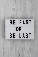 'Be Fast or Be Last' on a lightbox on a white wooden background, top view. Flat lay, overhead, from above.