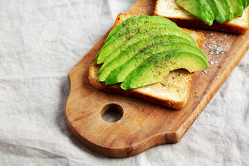 Homemade Avocado Toast on a rustic wooden board, side view. Copy space.