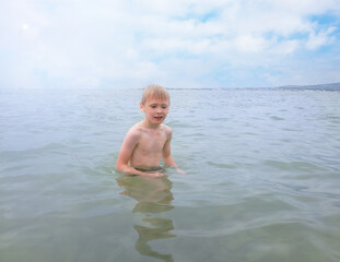 a boy swims in the sea against a blue sky with clouds