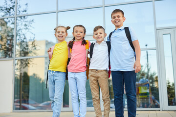 Obraz premium Smiling kids with backpacks standing near modern building
