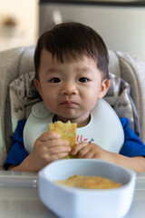 Adorable joyful and Happy 1 years old Chinese baby boy having food while sit on baby chair