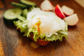 Poached egg on toast with herbs and vegetables on a wooden background