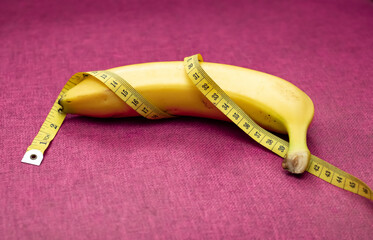 Men's health concept. A banana and a yellow measuring tape surround it. Magenta colour as background. 	
