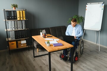 Disabled Businessman Sitting In Wheelchair Using Computer At Workplace