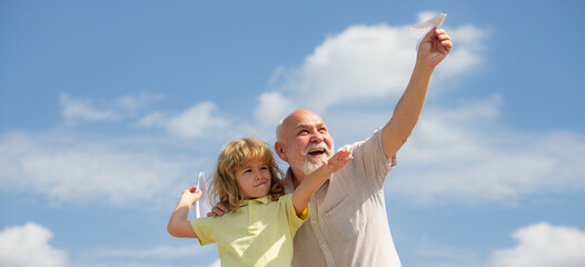 Grandfather and son with paper plane over blue sky and clouds. Men generation granddad and grandchild. Banner with copy space.